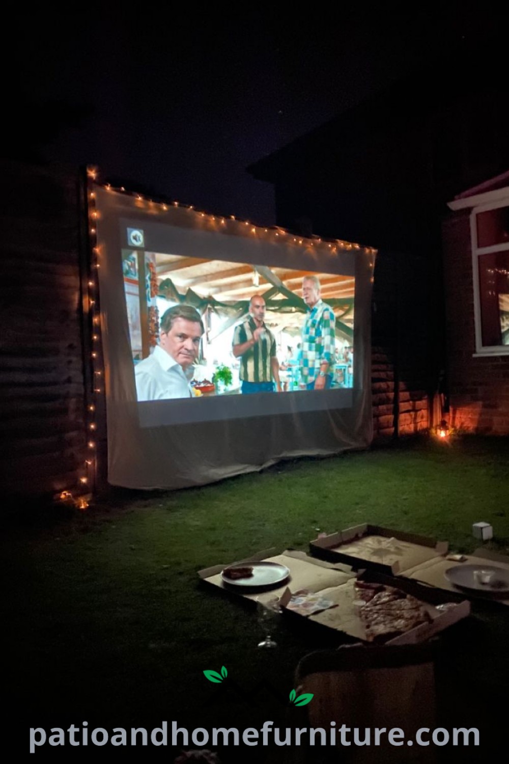 Outdoor movie screen set up in a dark garden, featuring laid-out snacks on the ground, surrounded by cozy decorations and a warm atmosphere, ideal for a memorable movie night experience, as featured on wellnesswink.com.