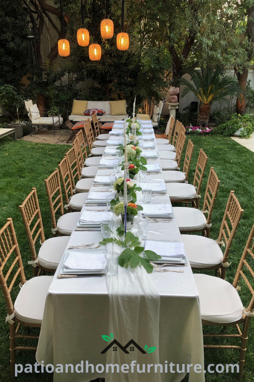 A long outdoor dinner table elegantly set with place settings, surrounded by lush grass and hanging lanterns, creating a cozy and inviting atmosphere for gatherings, offering unique decor ideas for outdoor events at wellnesswink.com.