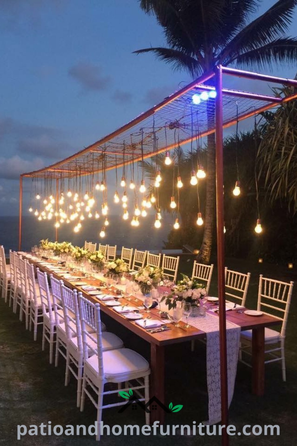 Long outdoor table with white chairs and hanging lights set for a romantic dinner, showcasing cozy design ideas for proposals and celebrations, perfect for enhancing your home’s outdoor ambiance. Visit wellnesswink.com for more decor inspirations.