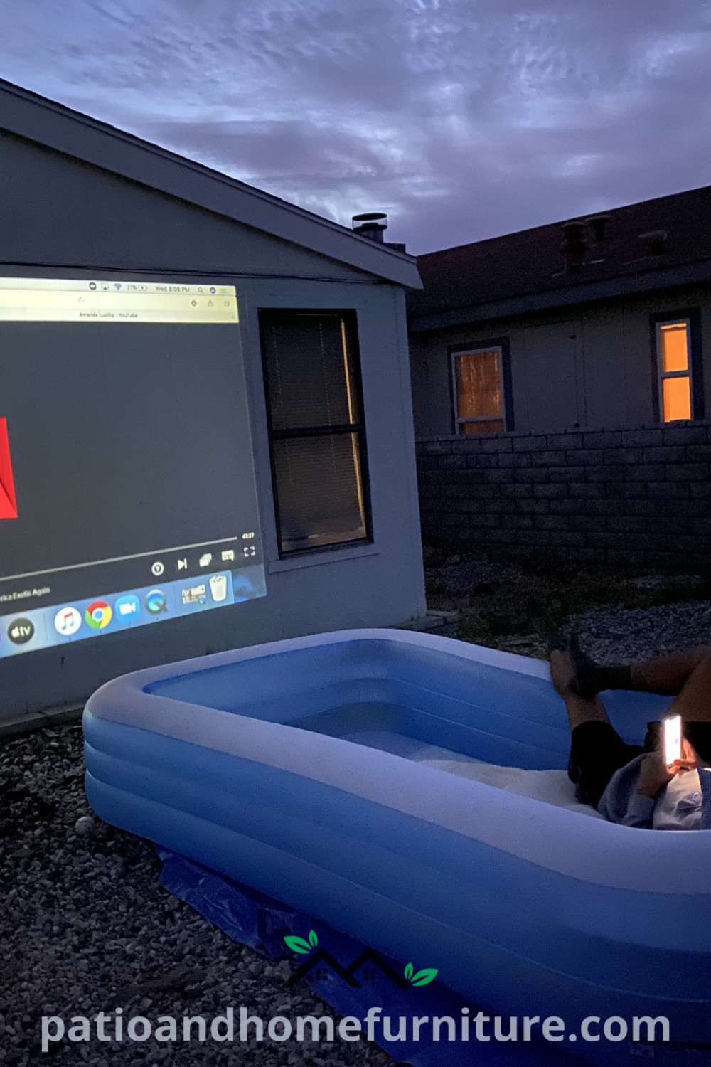A man sitting in an inflatable pool with a laptop on his lap, enjoying an outdoor movie night with a projector, surrounded by cozy decor ideas that inspire relaxation and fun, perfect for a unique backyard experience, featured on wellnesswink.com.