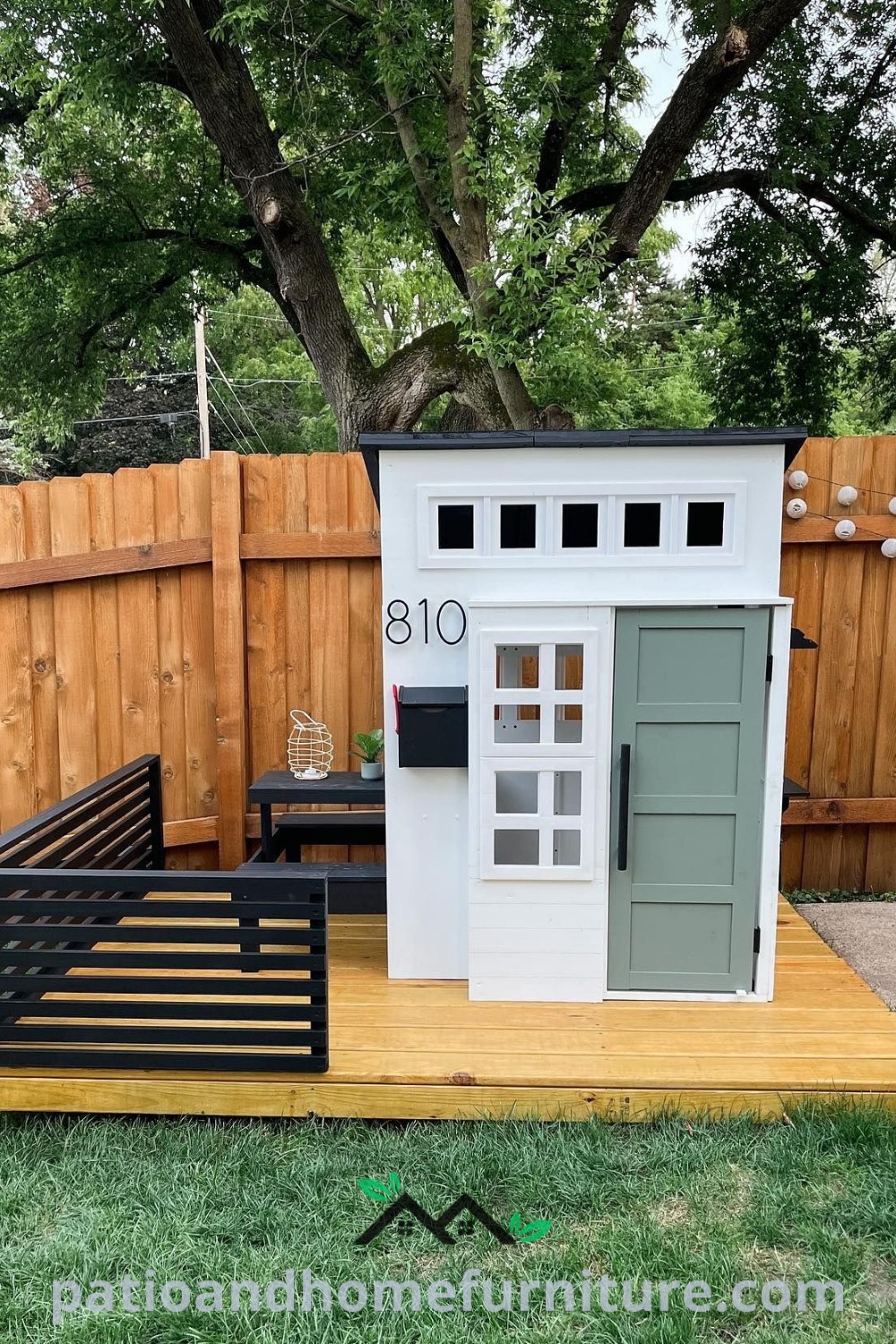 Small white playhouse on wooden platform beside green fence, creating a cozy backyard play area ideal for children, with design ideas and inspirations for enhancing outdoor spaces, featured on wellnesswink.com.