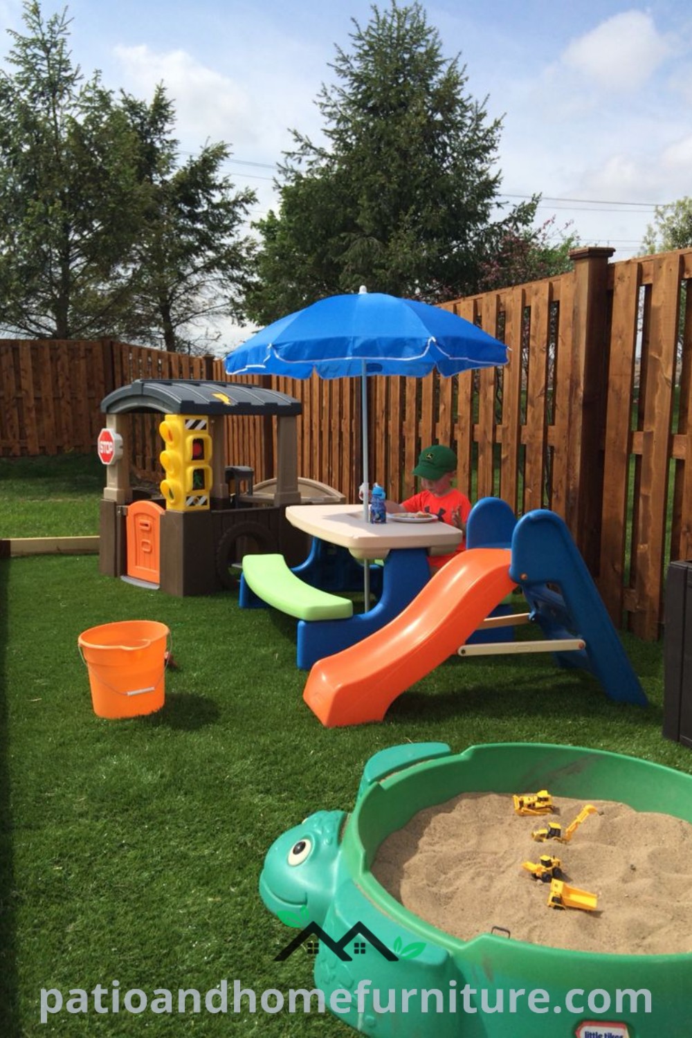 Outdoor toddler play area with sand, toys, and colorful umbrellas, set in front of a rustic wooden fence, providing a safe and inviting space for children to play in the sun, featuring cozy ideas from wellnesswink.com.