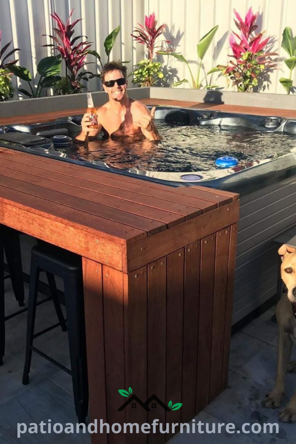 A man sitting in a hot tub beside a dog on the ground with its tongue out, set in a lush outdoor environment with cozy decor ideas, creating a serene atmosphere for relaxation. For more inspiring designs and cozy home ideas, visit wellnesswink.com.