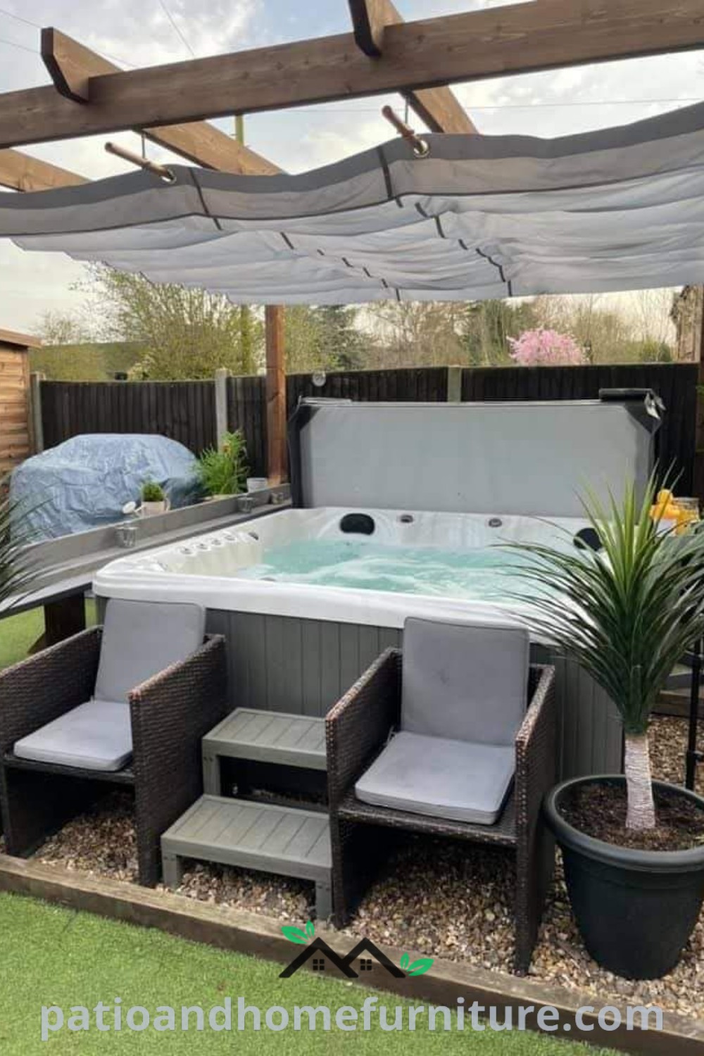 Outdoor hot tub surrounded by potted plants and chairs, with a covered patio area in the background, showcasing cozy design ideas for a tranquil backyard space, featured on wellnesswink.com.