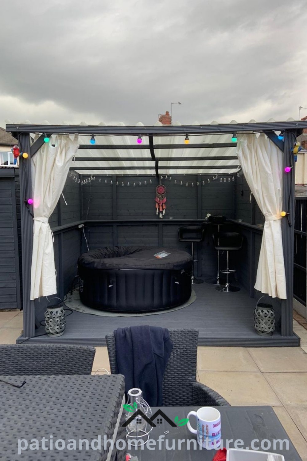 Outdoor hot tub area with sheer curtains, twinkling lights, and surrounding patio furniture, creating a cozy and inviting atmosphere for relaxation and outdoor enjoyment, featuring inspiring decor ideas from wellnesswink.com.