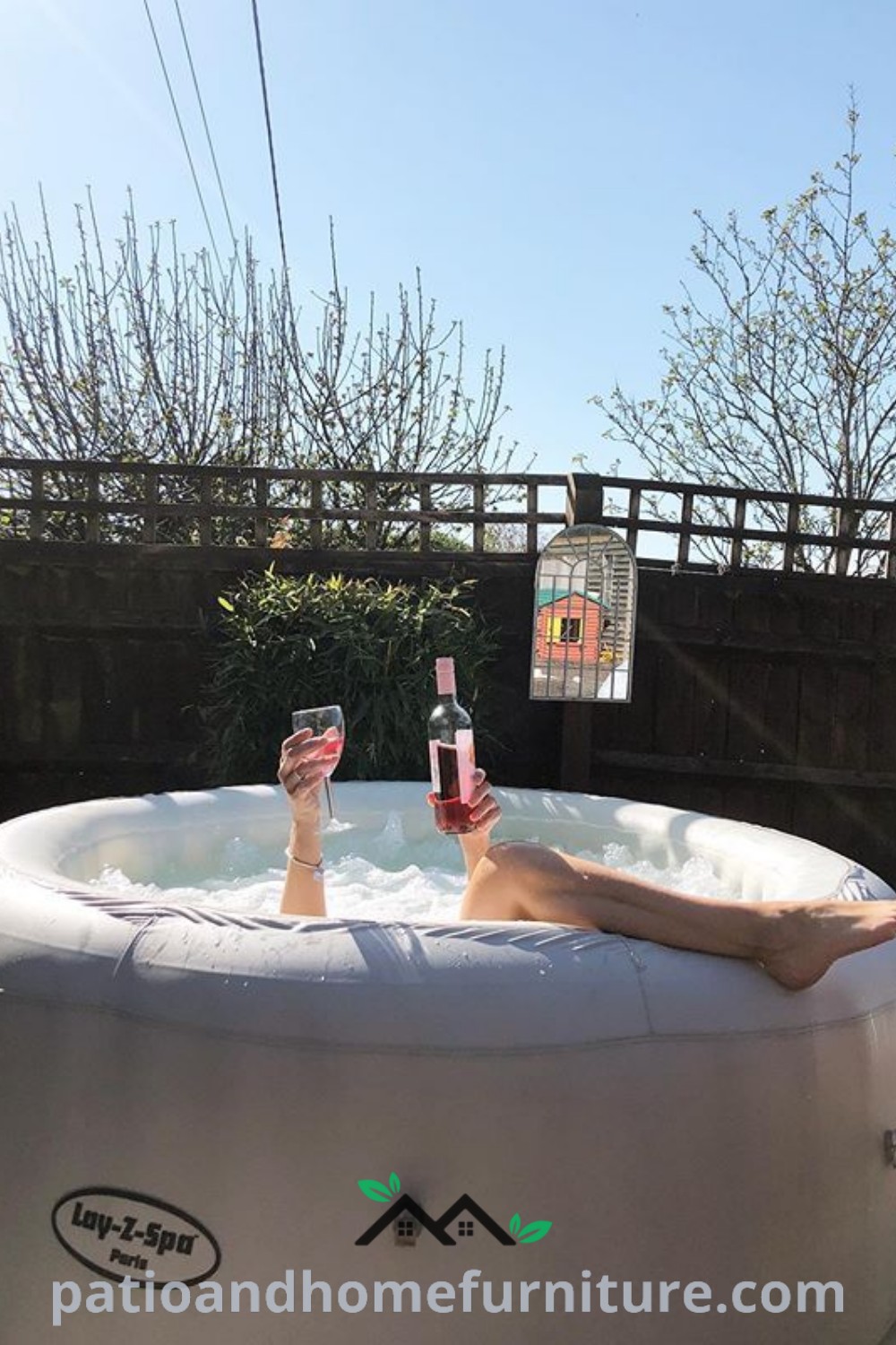 Person relaxing in an inflatable hot tub on a balcony with a bottle of wine and two glasses, surrounded by inviting decor, creating a cozy and serene atmosphere, featured on wellnesswink.com.