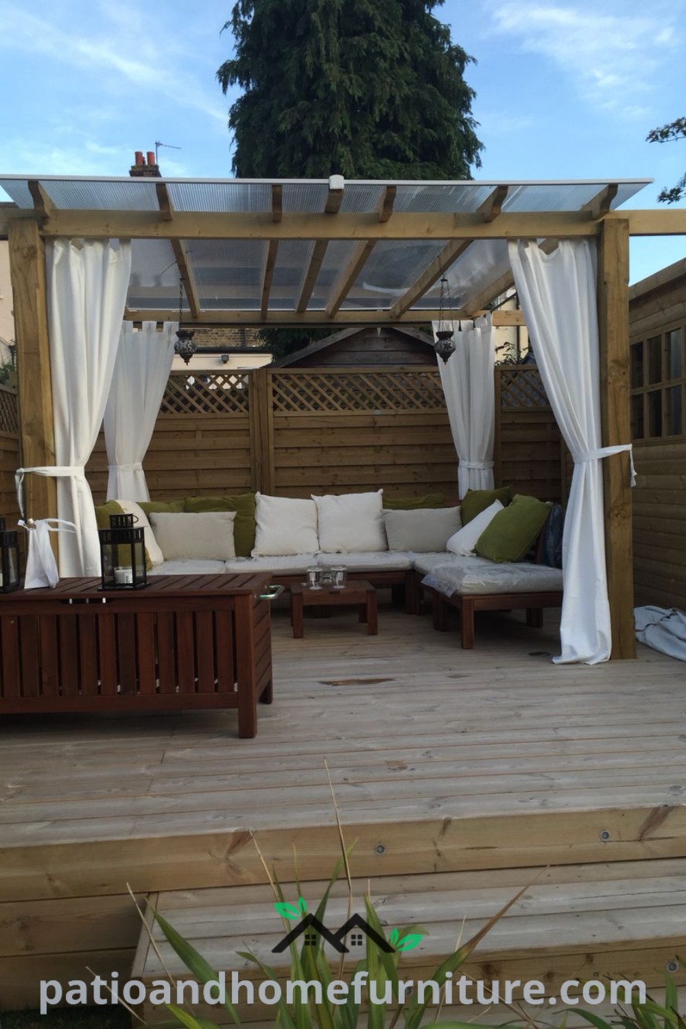 Cozy outdoor living area with comfy couches, decorative curtains on a pergola, and wooden decking, providing a stylish space for relaxation and entertainment, featuring string lights for added ambiance, from wellnesswink.com.